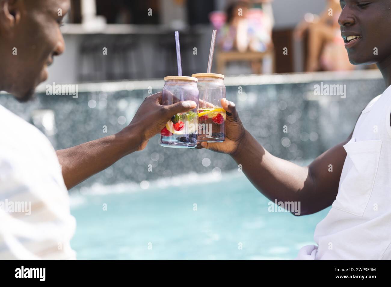 Zwei afroamerikanische Männer stoßen am Pool mit Früchten an Stockfoto