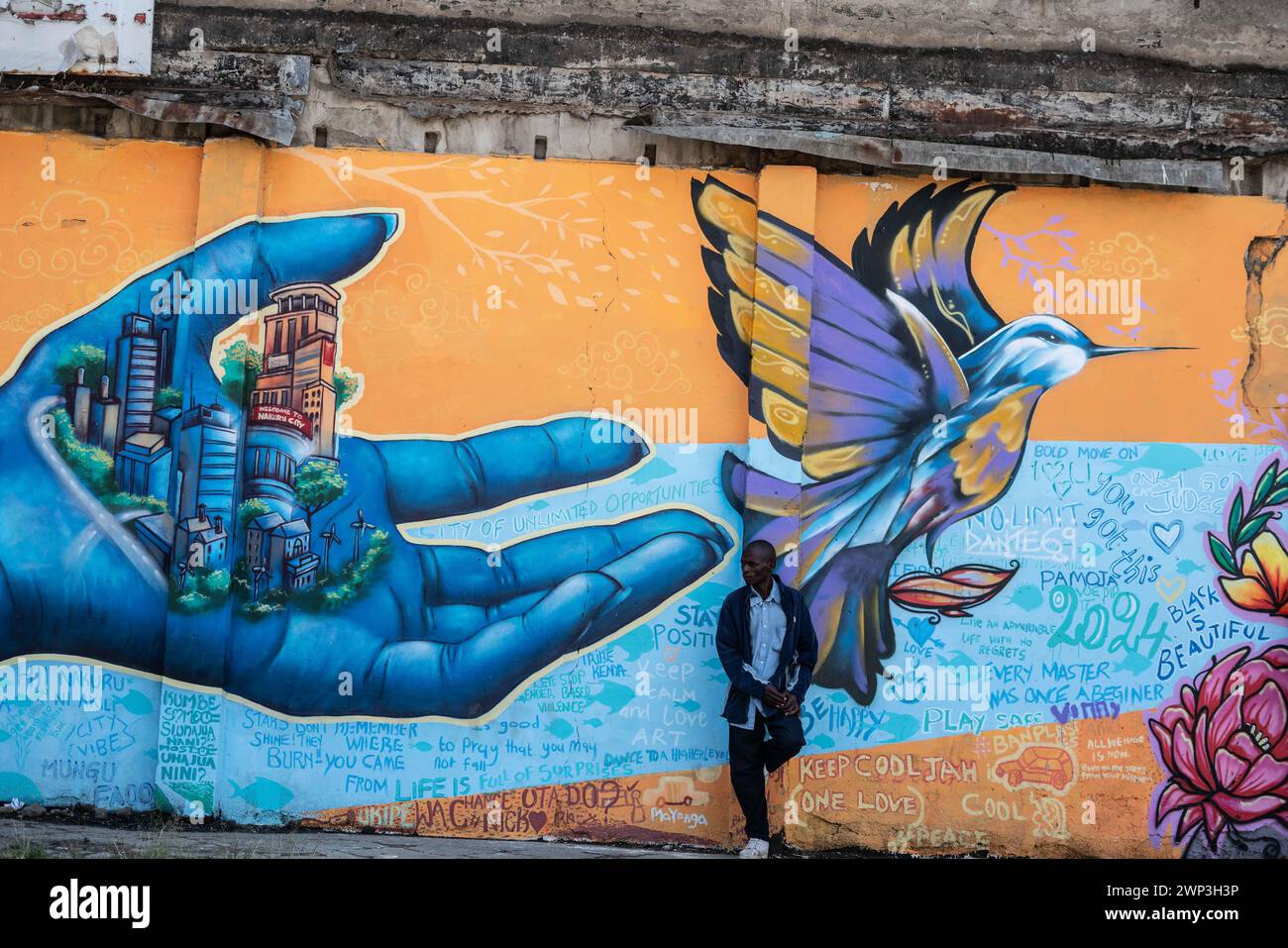 Nakuru, Kenia. März 2024. Ein Mann steht vor einem Wandbild, das eine Hand in der Hand einer Stadt und einen fliegenden Vogel zeigt, gemalt an einer Wand in Nakuru Town, das als Teil des UNESCO-Projekts „Creative City“ von Nakuru geschaffen wurde, um das kulturelle und künstlerische Erbe der Stadt zu präsentieren. Das kollaborative Werk enthält Beiträge verschiedener Graffiti-Künstler, darunter BankSlave, Joel Bergner, Chelwek, Dante und Natasha Floortje. (Foto: James Wakibia/SOPA Images/SIPA USA) Credit: SIPA USA/Alamy Live News Stockfoto