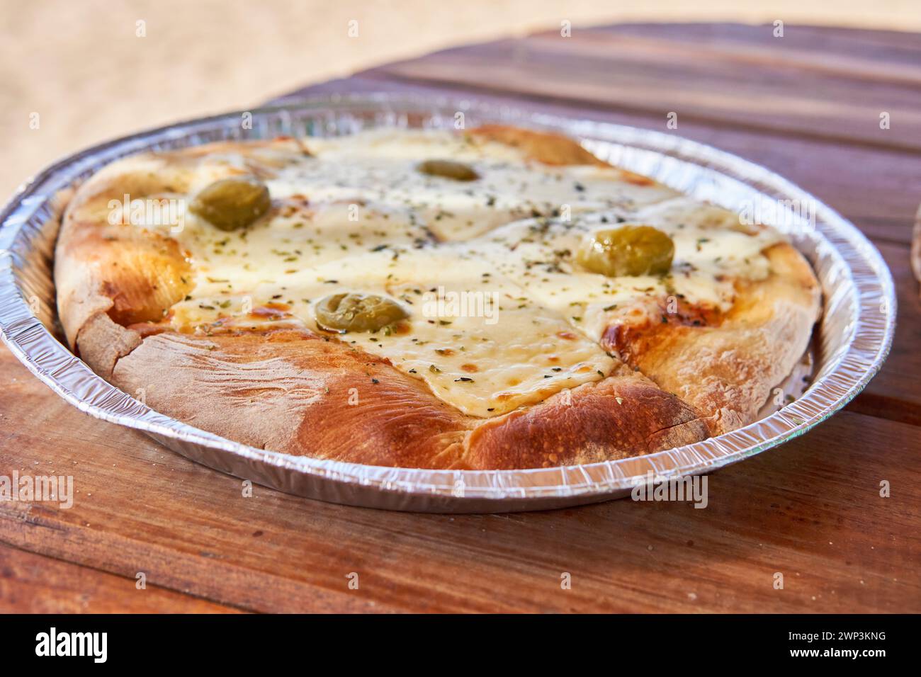 Pizza mit Mozzarella und Oliven auf einem Aluminiumtablett auf einem Holztisch, Fast Food für einen Sommertag am Strand oder am Fluss Stockfoto