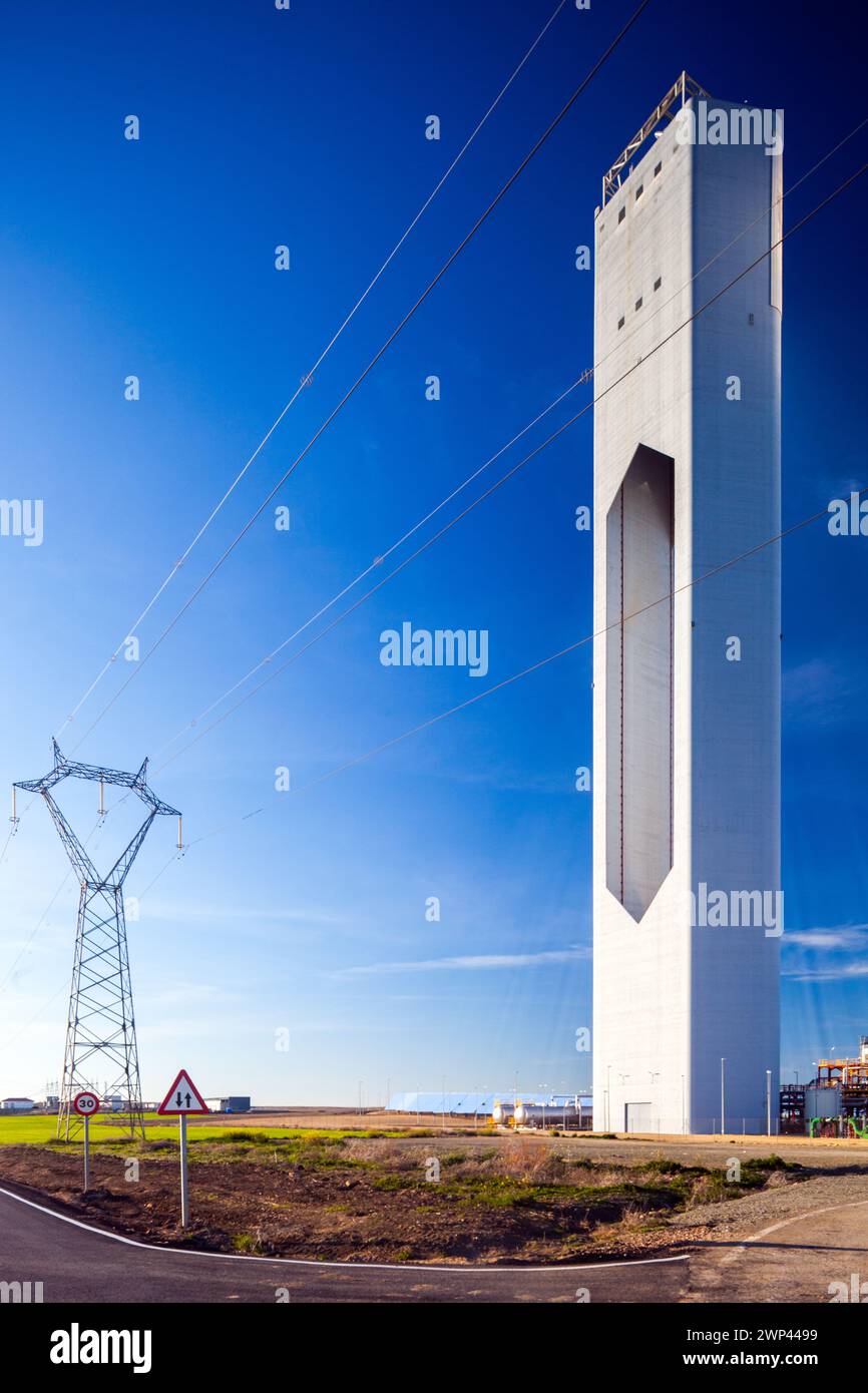 Hochspannungsleitungen, die neben einer hochaufragenden Solaranlage unter blauem Himmel verlaufen. Stockfoto