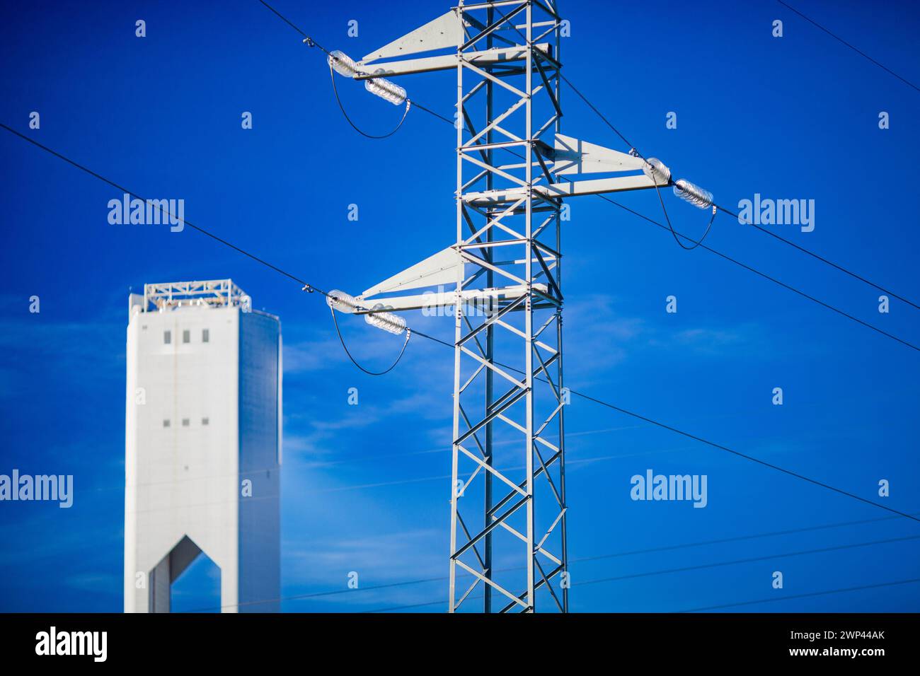 Hochspannungsleitungen, die neben einer hochaufragenden Solaranlage unter blauem Himmel verlaufen. Stockfoto