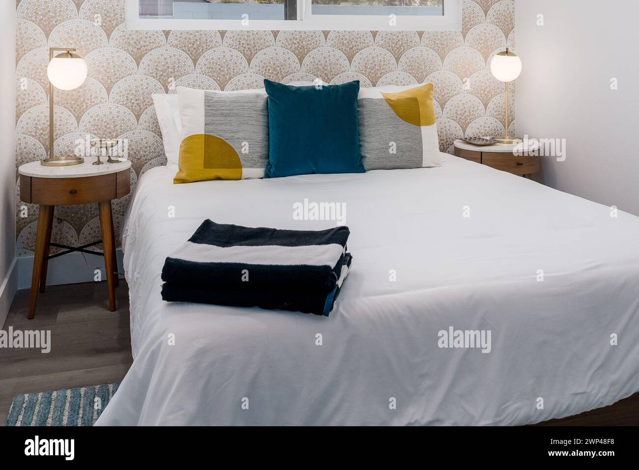 Modernes Gästezimmer mit bequemem Bett, Kissen, Nachttischen und Mosaikfliesen Stockfoto