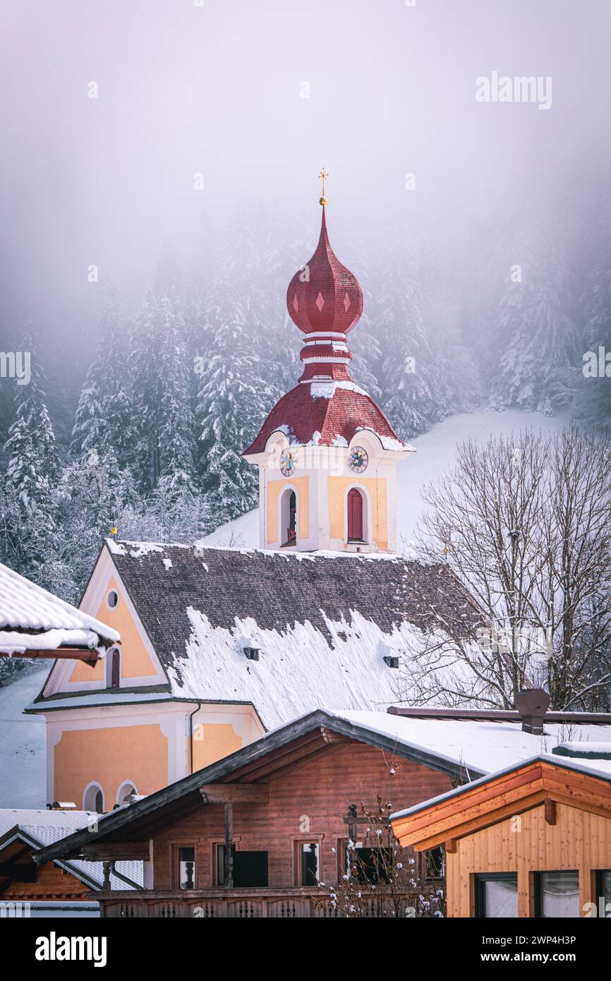 Ein Dorf im Winter mit einer roten Kuppelkirche vor einem schneebedeckten Wald, The Mountain Doctor, Going, Austria Stockfoto