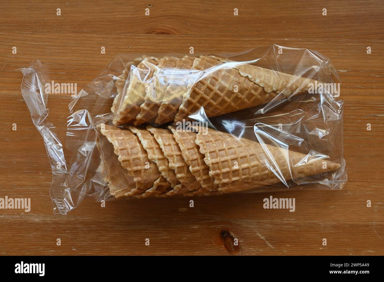 Waffelkegel in Plastikverpackung auf einem Holztisch, fertig mit köstlichem Eis gefüllt Stockfoto