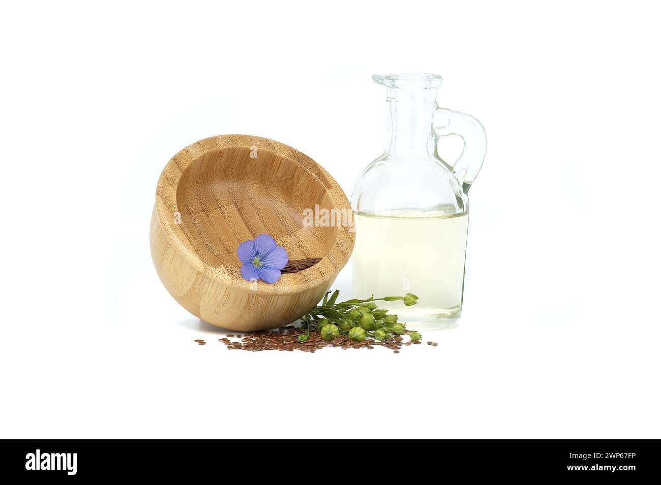 Holzmörtel gefüllt mit kleinen braunen Leinsamen und einer blauen Leinpflanze blüht neben Leinöl in Glasdekanter isoliert auf weißem Hintergrund Stockfoto