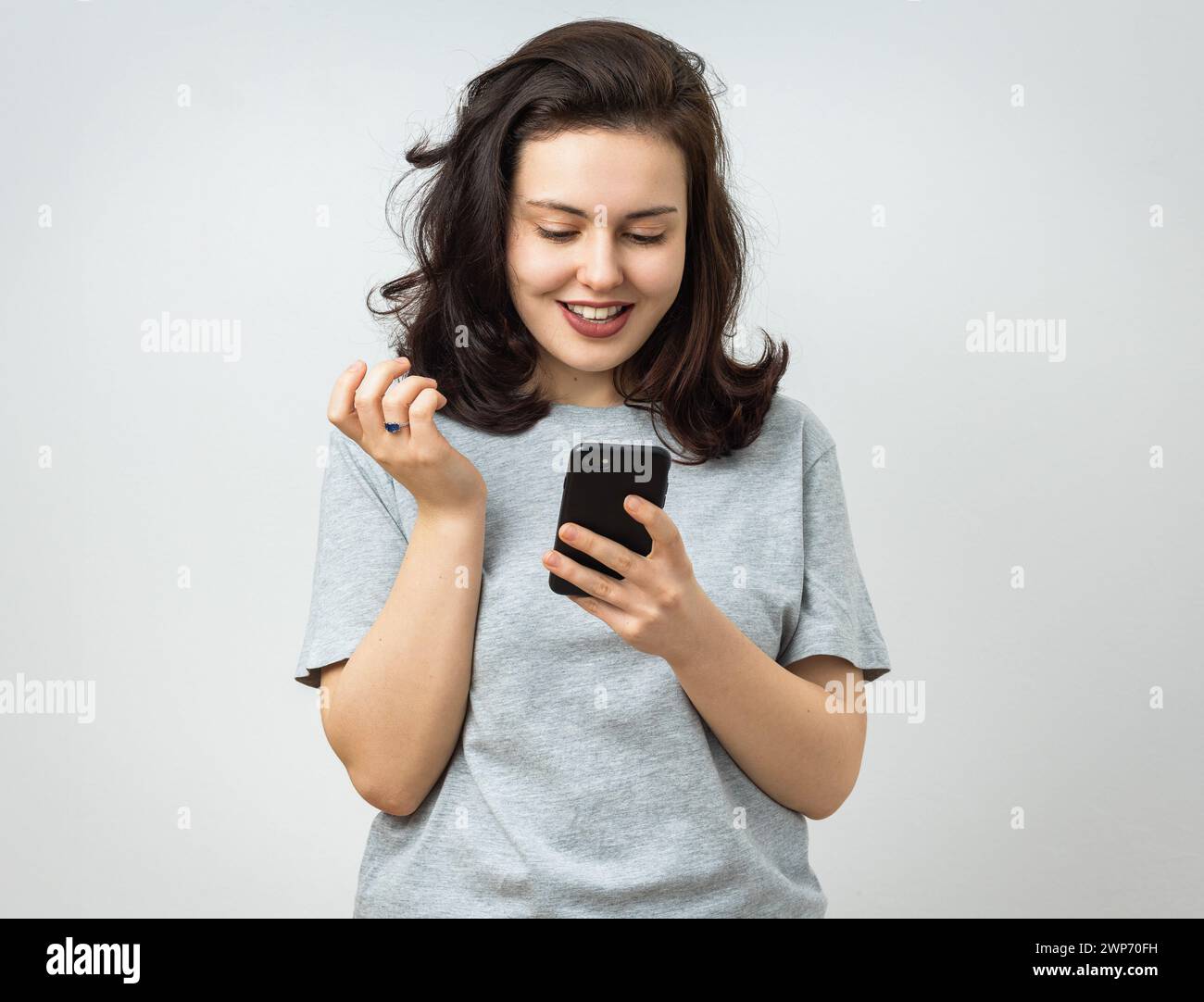 Attraktive junge Frau, die glücklich auf den Bildschirm ihres Smartphones blickt. Isoliert auf grauem Hintergrund Stockfoto