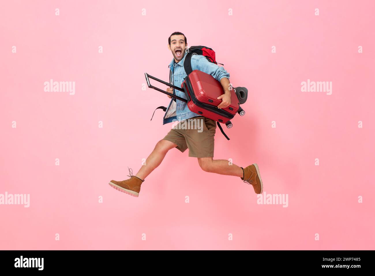 Bereit zu fliegen ekstatisch überraschter Touristenmann, der Gepäck hält und in rosa Farbe springt isolierte Hintergrundaufnahme im Studio Stockfoto