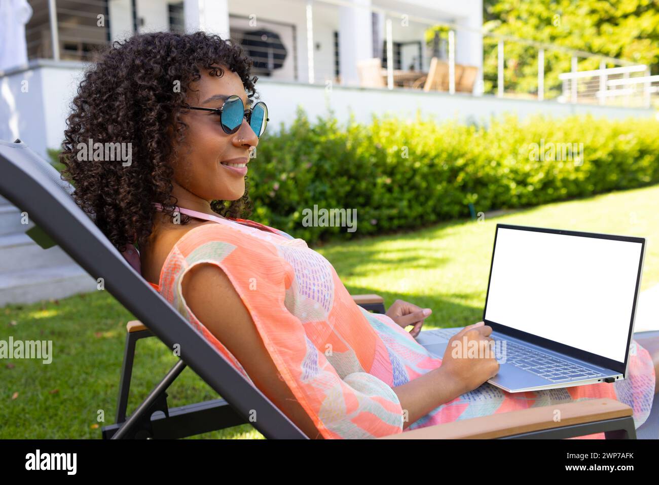 Eine Frau mit Sonnenbrille arbeitet an ihrem Laptop, während sie draußen mit Kopierraum sitzt Stockfoto