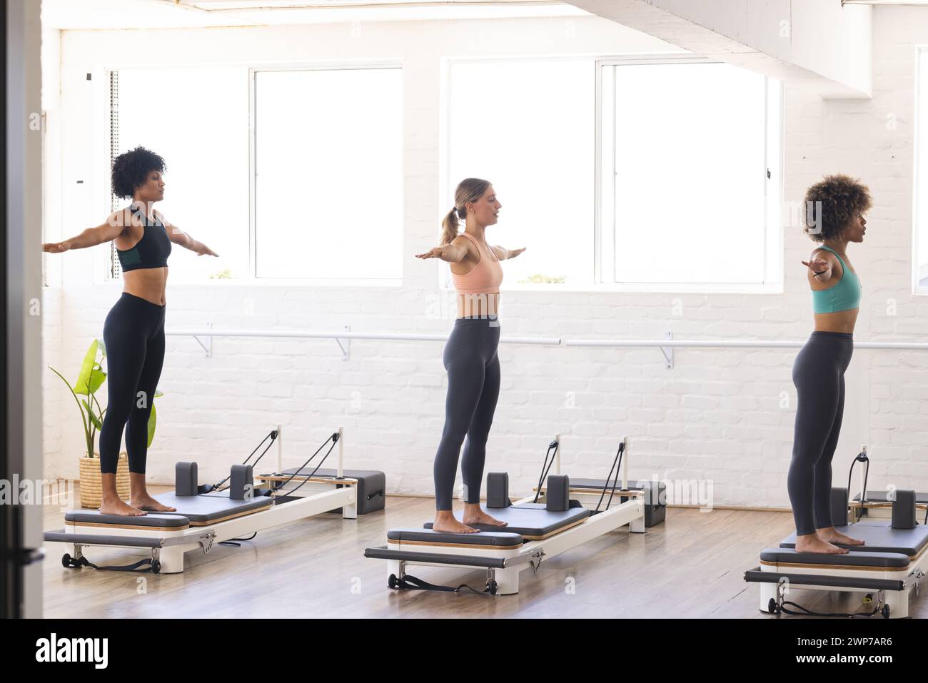 Verschiedene Frauen üben Pilates auf Reformern in einem hellen Atelier aus Stockfoto