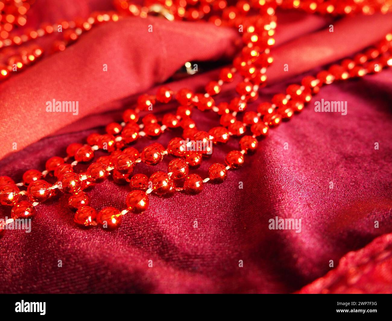 Rote, schöne Perlen auf hellem Scharlachsamt. Schöner luxuriöser Damenschmuck auf weichem Stoff. Flach liegend in Nahaufnahme. Damenkram und Kosmetik Stockfoto