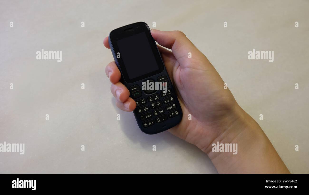 Hand hält ein schwarzes, veraltetes Handy mit leerem Bildschirm. Stockfoto