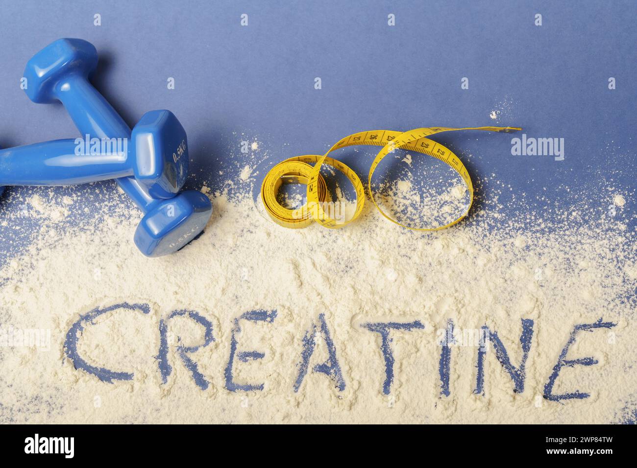 Wort Kreatin auf Kreatinpulver auf blauem Hintergrund, mit Kurzhanteln und Maßband Stockfoto