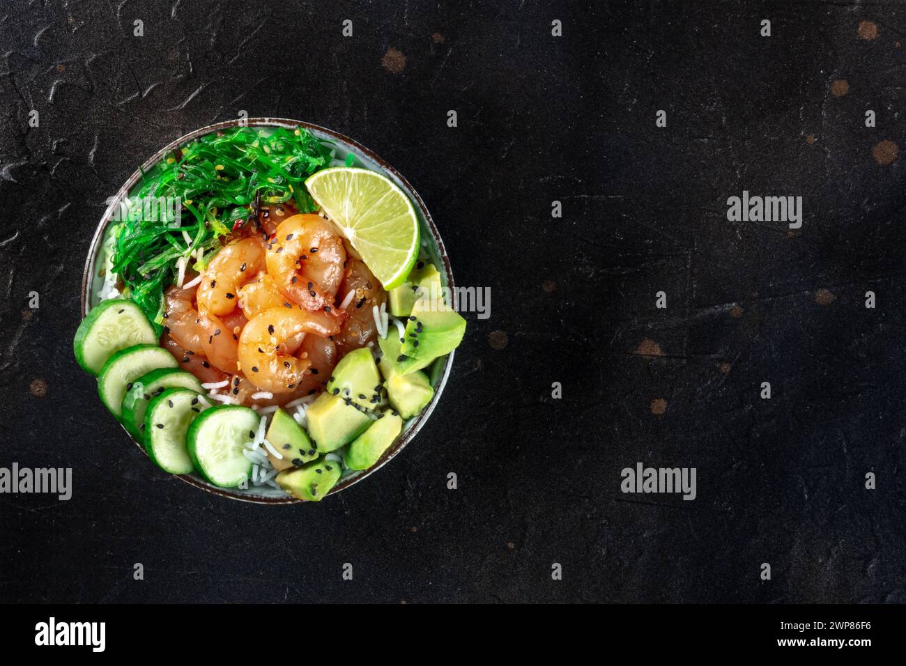 Shrimps Poke Bowl mit Avocado, Gurken, Wakame und Limette, von oben auf schwarzem Hintergrund mit einem Platz für Text Stockfoto