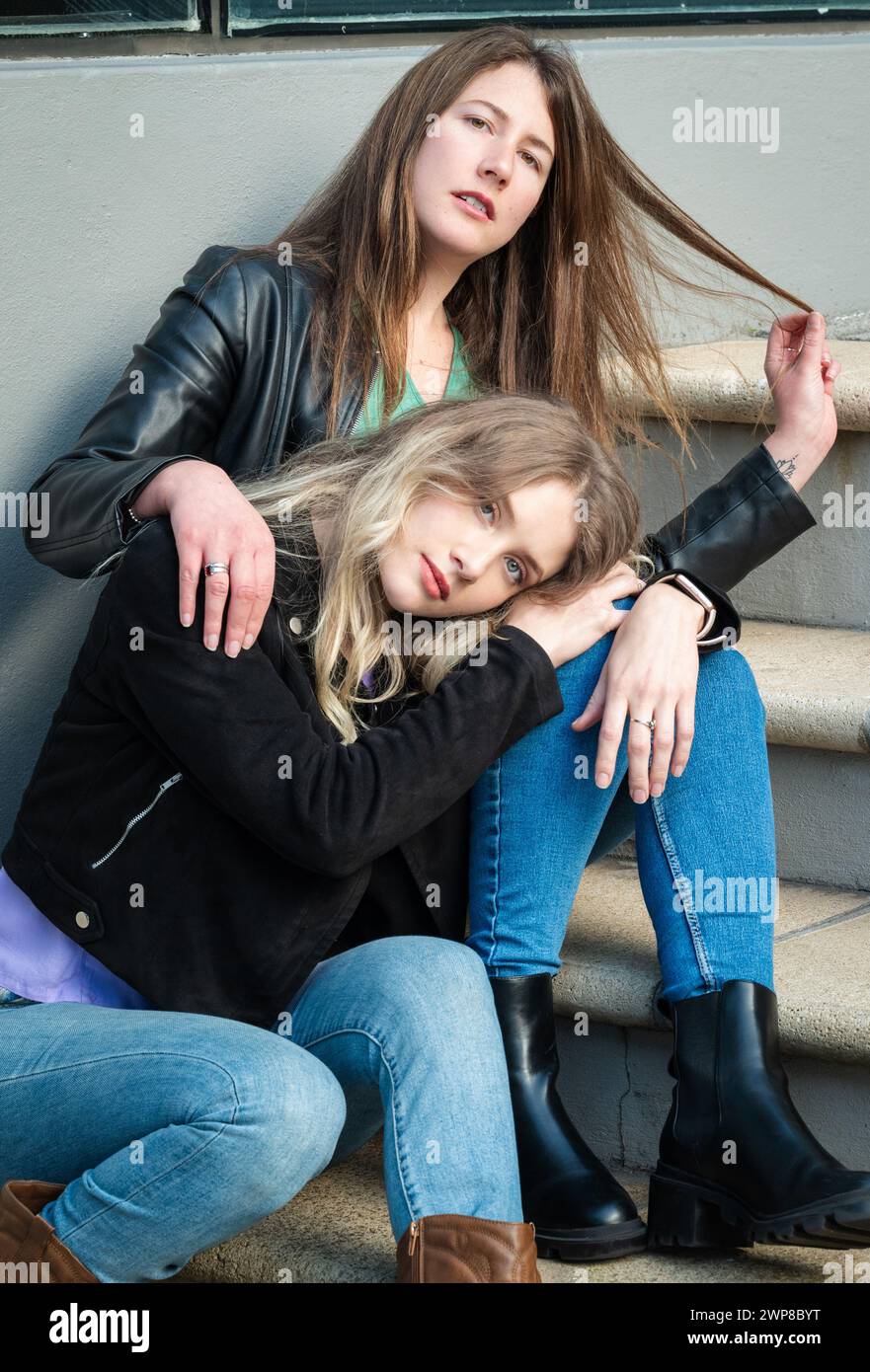 Zwei Mädchen, eine Brünette und eine Blondine, sitzen auf der Stadtreppe Stockfoto