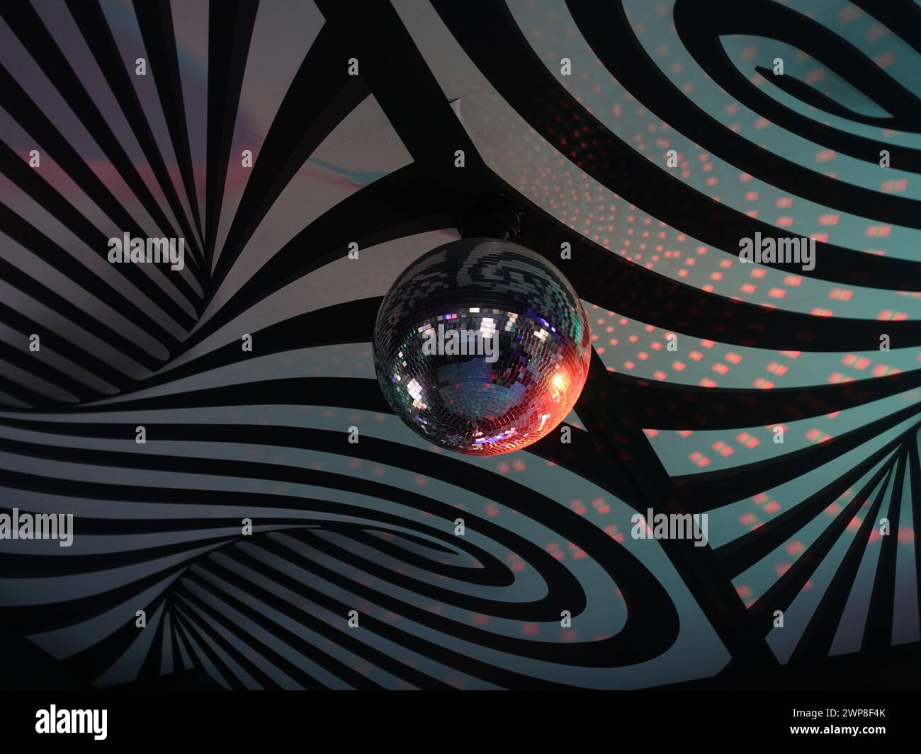 Eine glitzernde Discokugel hängt an einer wirbelnden Decke Stockfoto