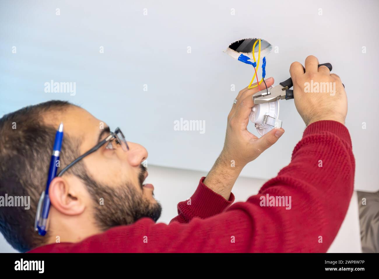 Junger Mann, der den Deckenstrahler repariert, der den Schäler hält, um Drähte zu schneiden und sie mit neuen zu befestigen Stockfoto