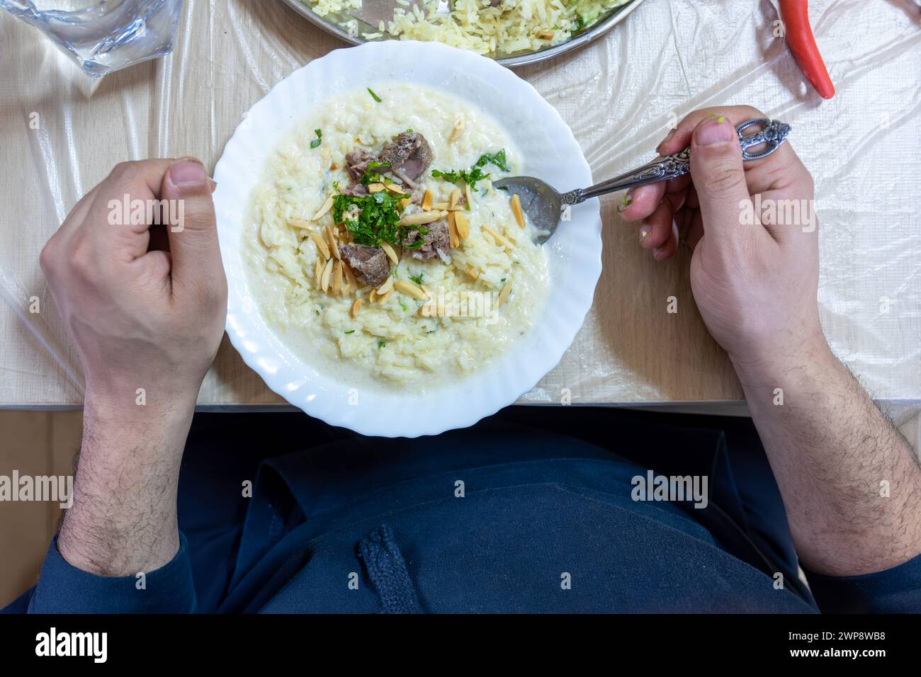 Männliche Hände mit Mansaf, während er seinen Teller mit Fleisch, Reismarmelade, Nüssen und Petersilie während des iftar im ramadan zubereitete Stockfoto