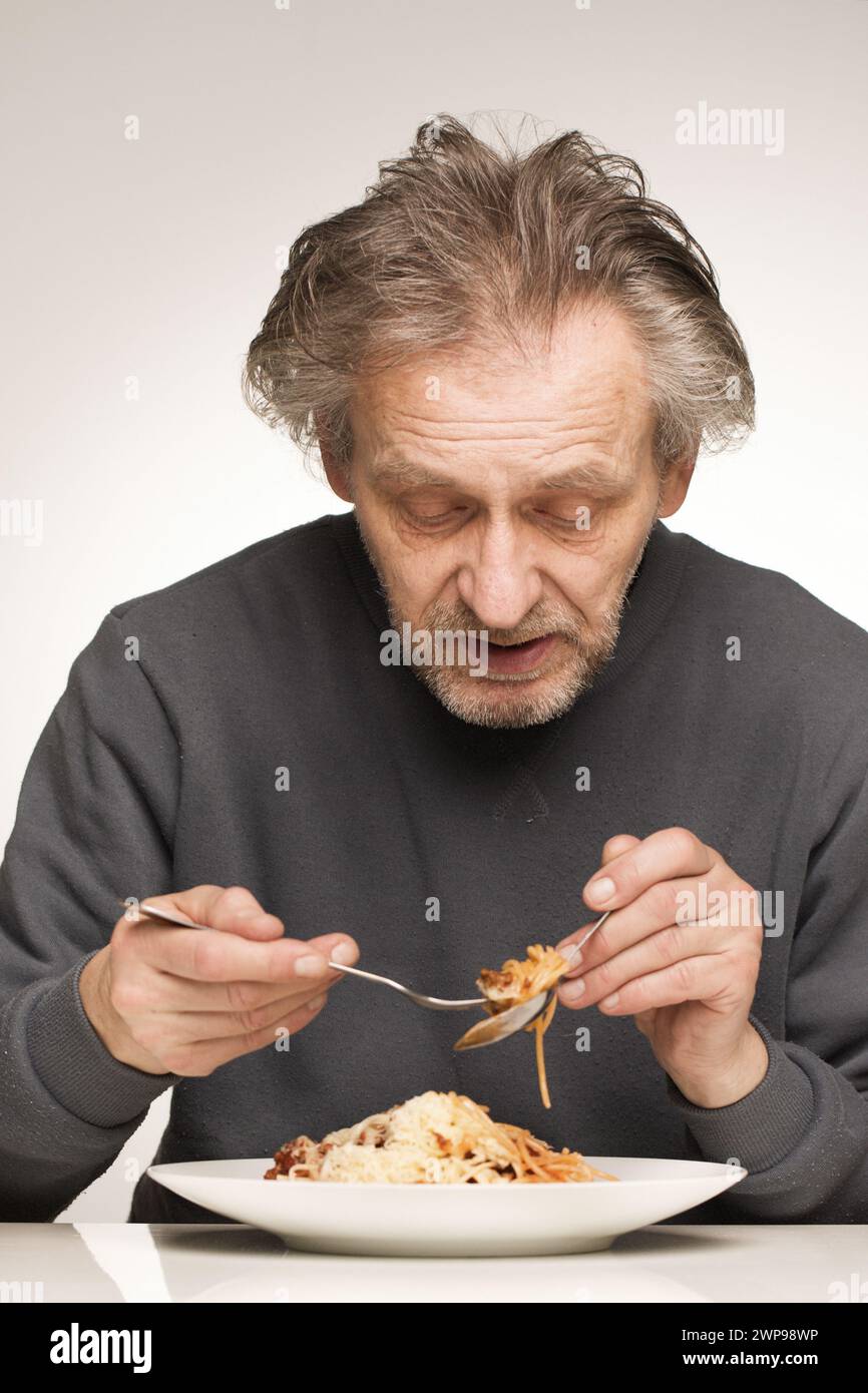 Ein älterer Mann isst Spaghetti mit Hackfleisch, Tomaten und Käse Stockfoto