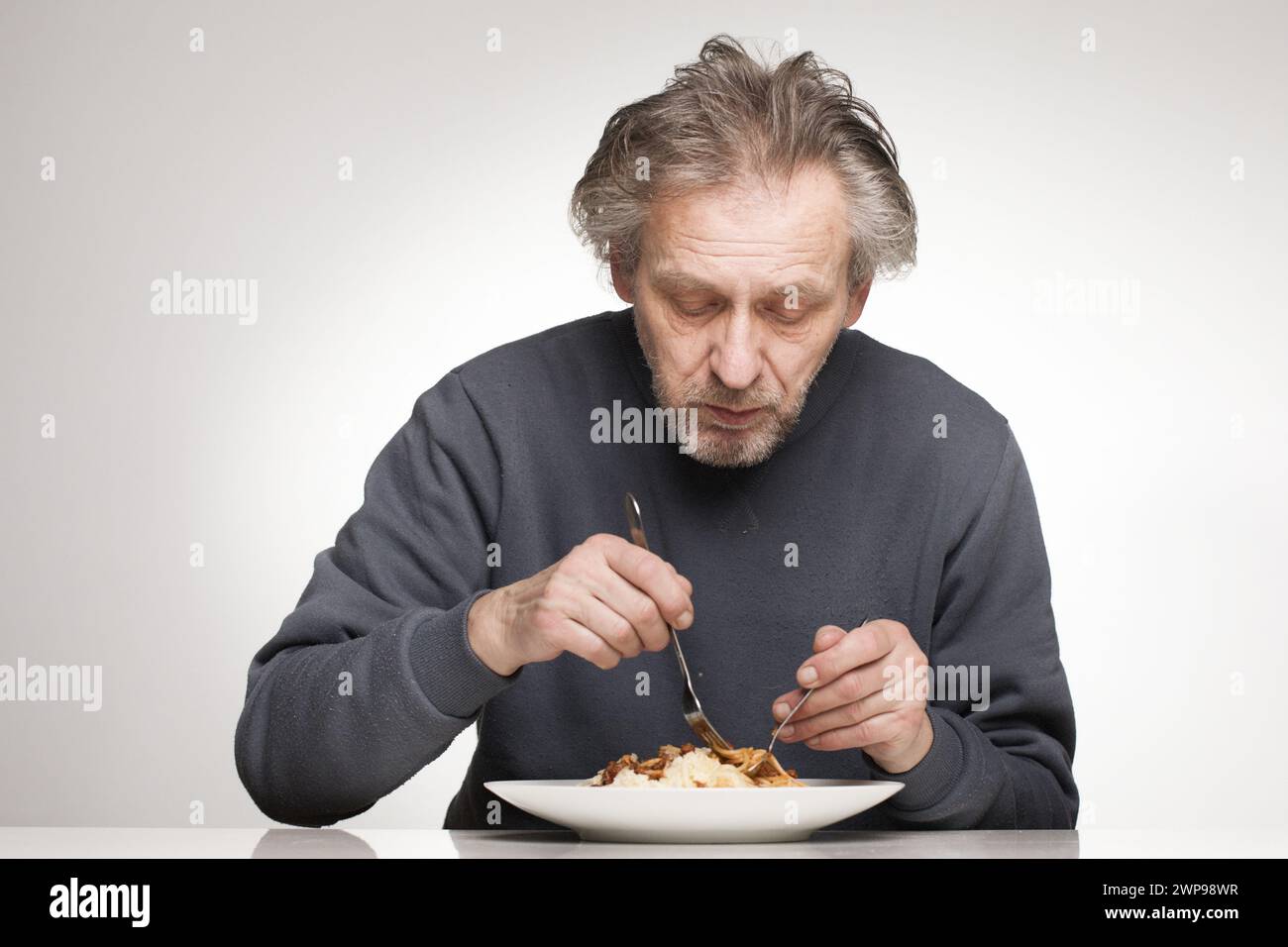 Ein älterer Mann isst Spaghetti mit Hackfleisch, Tomaten und Käse Stockfoto