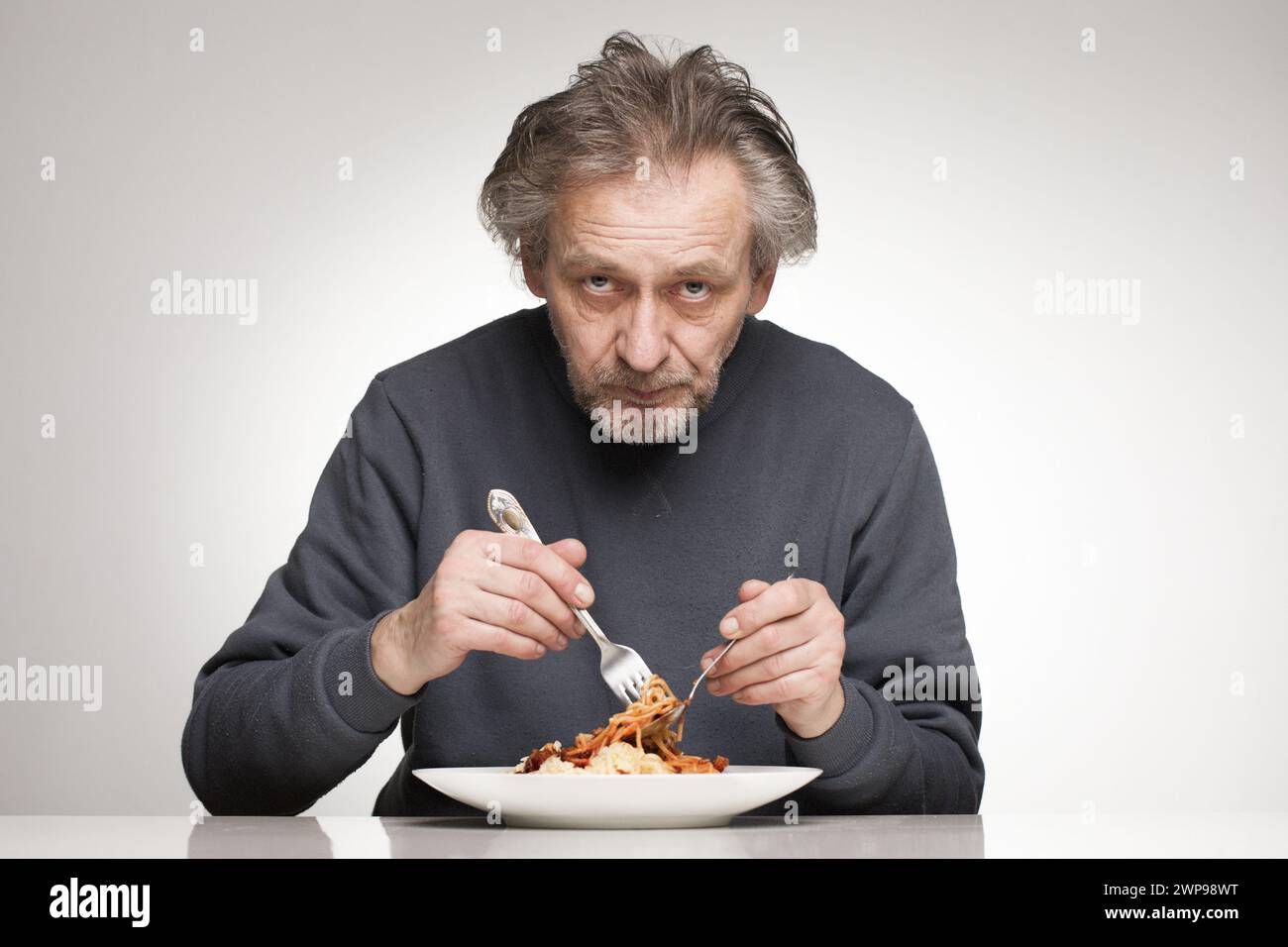 Ein älterer Mann isst Spaghetti mit Hackfleisch, Tomaten und Käse Stockfoto