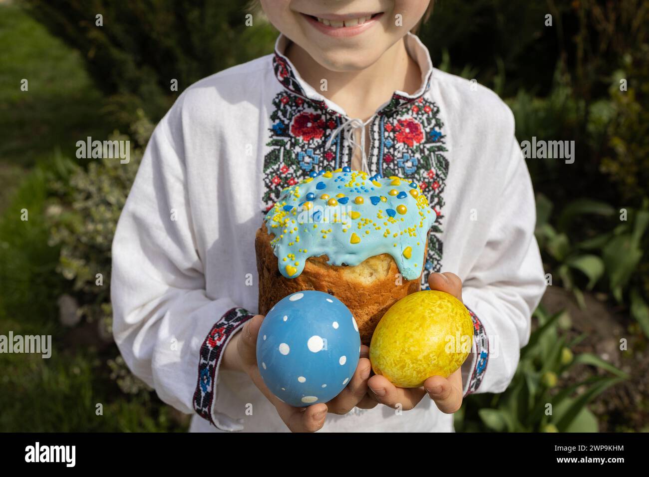 Ukrainisches Kind in einem gestickten Kleid hält einen Ostercupcake und Eier in gelben und blauen Farben. Osterkonzept. Familientradition. Christus i Stockfoto