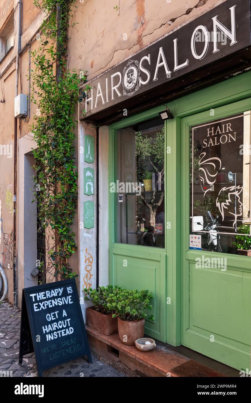 Friseursalon, Eingangstür zum Haidresserladen für Männer und Frauen im Trastevere-Viertel. Ironisches Nachrichtenbanner draußen. Rom, Italien, Europa, EU Stockfoto