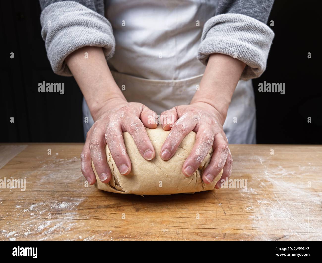 Ein Nahfoto einer Frau, die eine große Kugel Teig auf einem hölzernen Schneidebrett kneten. Stockfoto