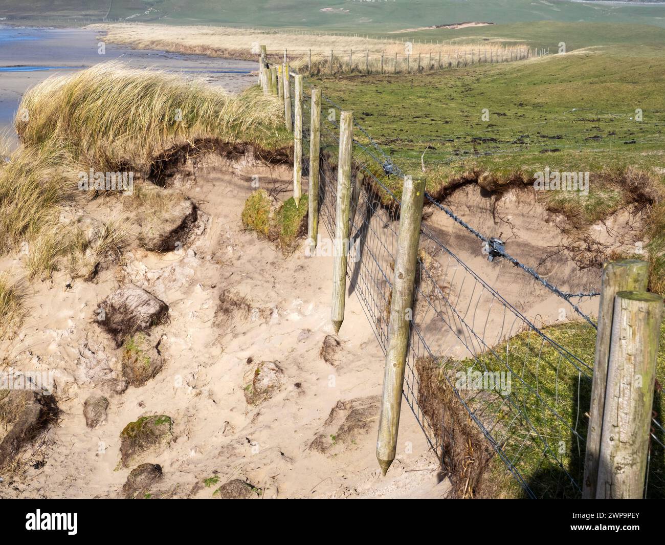 Ein Zaun hing, als die Sanddünen in Machir Bay, in Islay, Schottland, von Sturmwellen erodiert wurden. Stockfoto