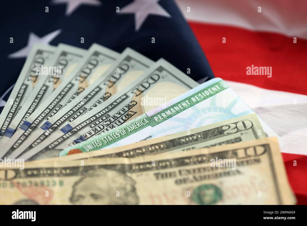 Green Card und Dollarscheine mit Wohnsitz in den Vereinigten Staaten von Amerika auf gefalteter US-Flagge in Nahaufnahme Stockfoto