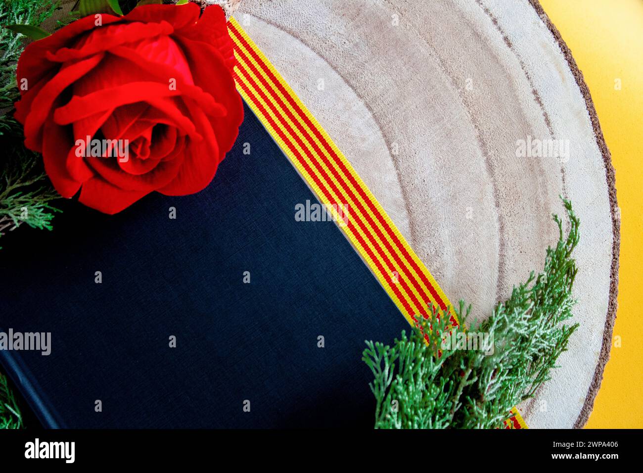 Schwarzes Cover-Buch mit einer roten Rose auf einem Holzstamm und einem Band der katalanischen Flagge Stockfoto