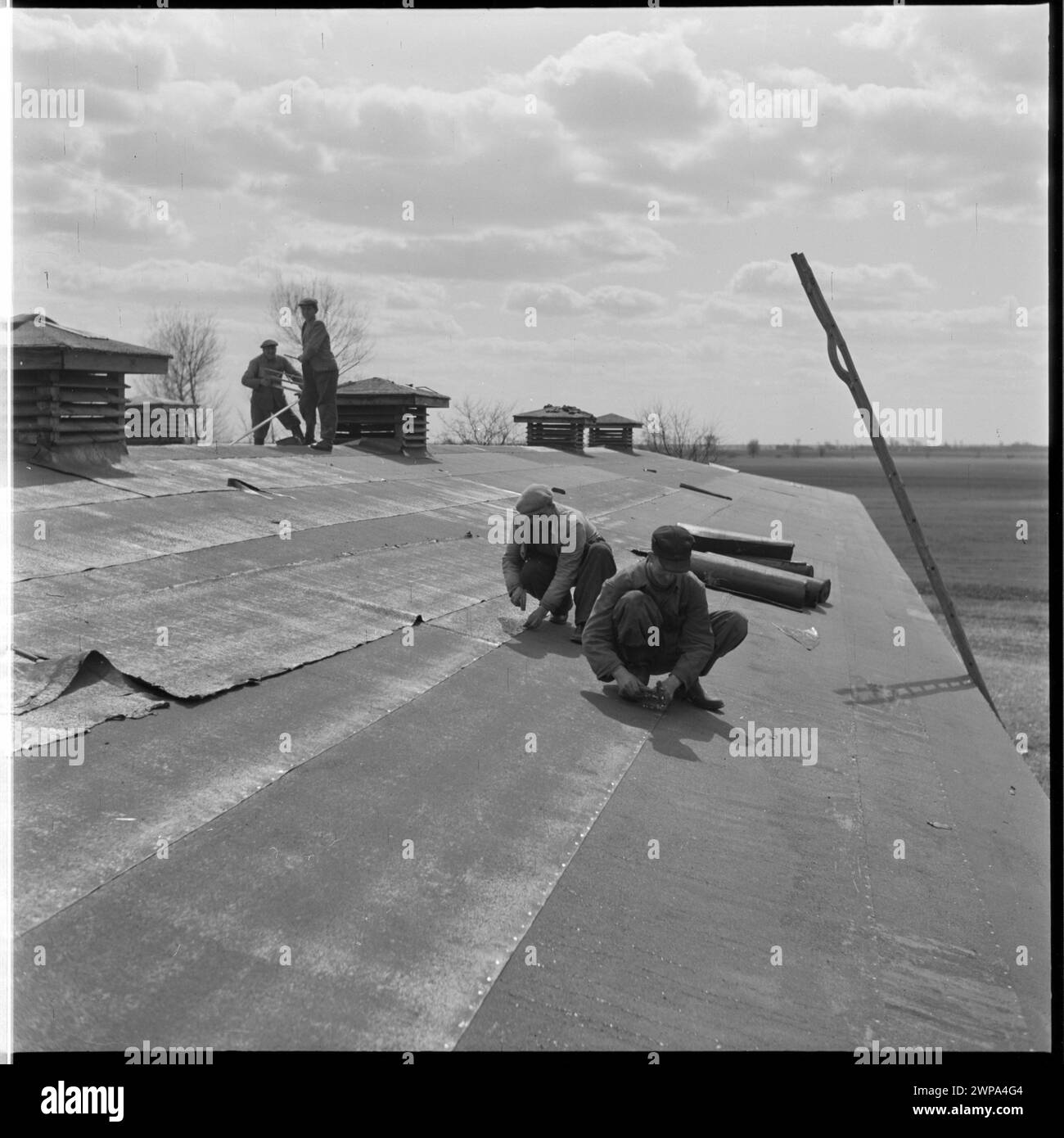Foto von Dachdeckern, die auf einem Gebäudedach bei PGR Karsk Pyrzycki im Jahr 1954 arbeiten, dokumentieren Nachkriegsarbeit und frühe Ursus-Traktorproduktion. Stockfoto
