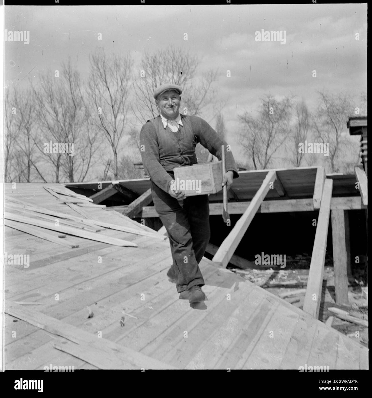 Schwarz-weiß-Bild eines Dachdeckers auf einem PGR Karsk Pyrzycki-Gebäudedach im Jahr 1954, das ländliche Arbeitskräfte und die frühe Ursus-Traktorproduktion veranschaulicht. Stockfoto