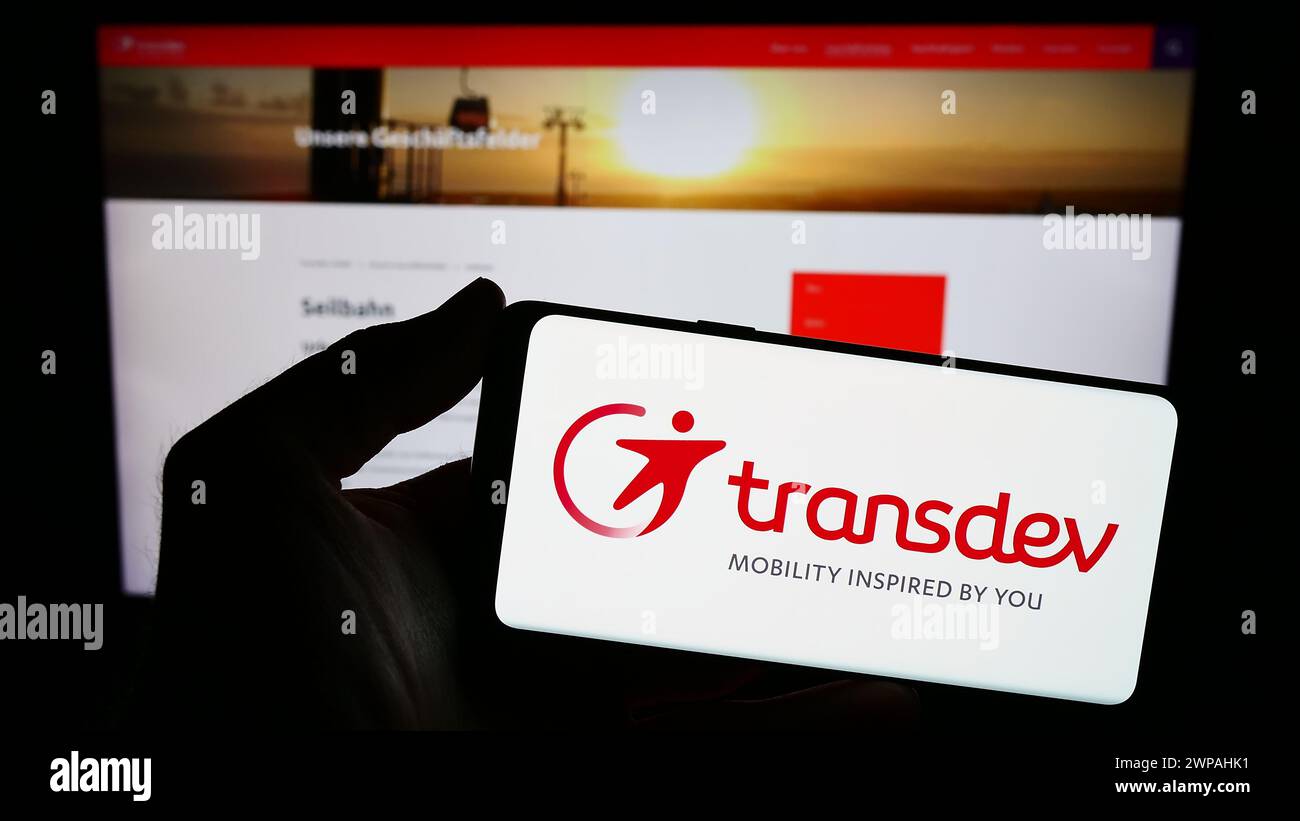 Person mit Smartphone mit Logo des deutschen Verkehrsunternehmens Transdev GmbH vor der Website. Schwerpunkt auf dem Display des Telefons. Stockfoto