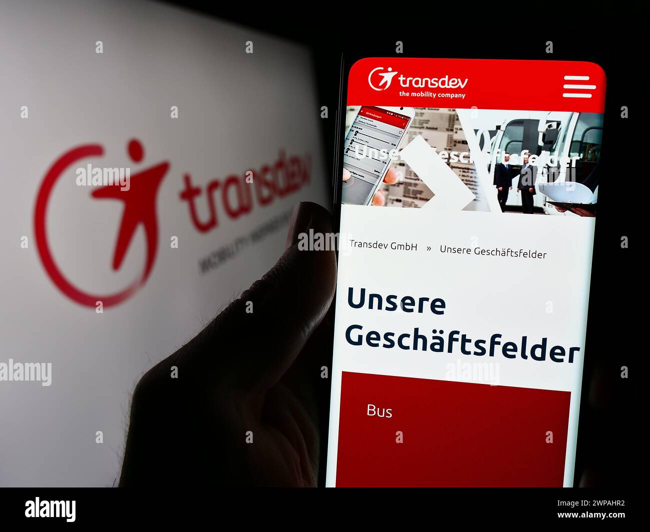 Person, die ein Mobiltelefon hält, mit der Webseite des deutschen Verkehrsunternehmens Transdev GmbH vor dem Logo. Konzentrieren Sie sich auf die Mitte des Telefondisplays. Stockfoto