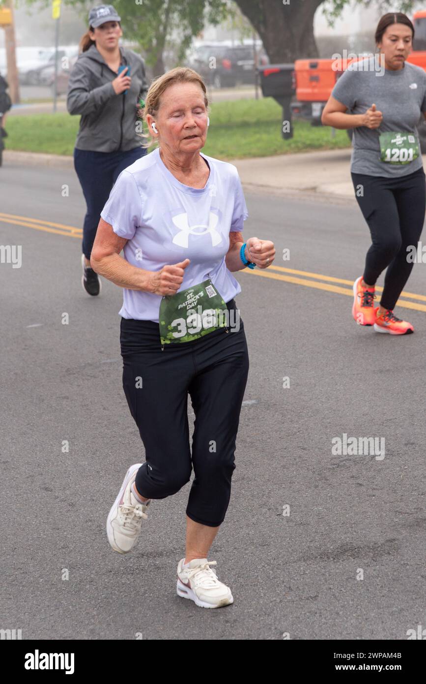 Eine fitte, ältere Frau, die müde aussieht, rennt in der St. Patrick's Day 5 km Run & Walk in Pharr, Hidalgo County, Texas, USA. Stockfoto