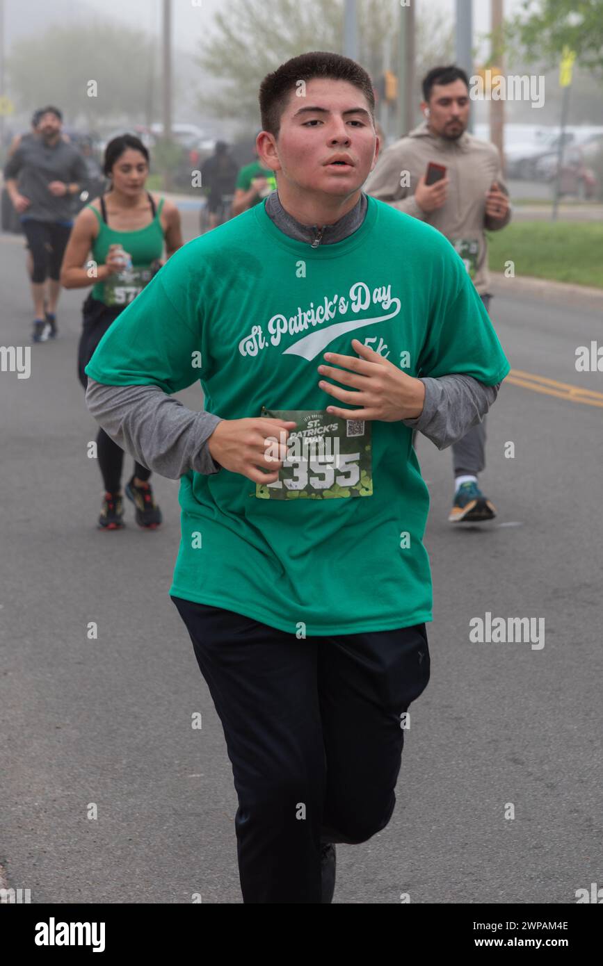 Ein junger Mann in einem grünen T-Shirt, der in der St. rennt Patrick's Day 5 km Run & Walk, kurz vor dem Ende des Rennens, Looking Fed, Pharr, Hidalgo County, Texas, USA. Stockfoto