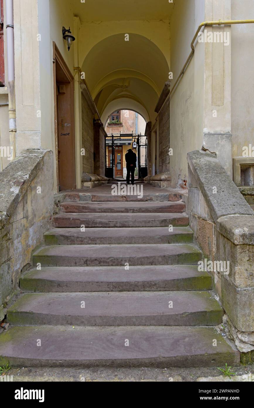 Ein Mann, der einen schmalen Gang mit alten, abgenutzten Treppen hinuntergeht, in der Stadt Lemberg, Ukraine, März 2024 Stockfoto