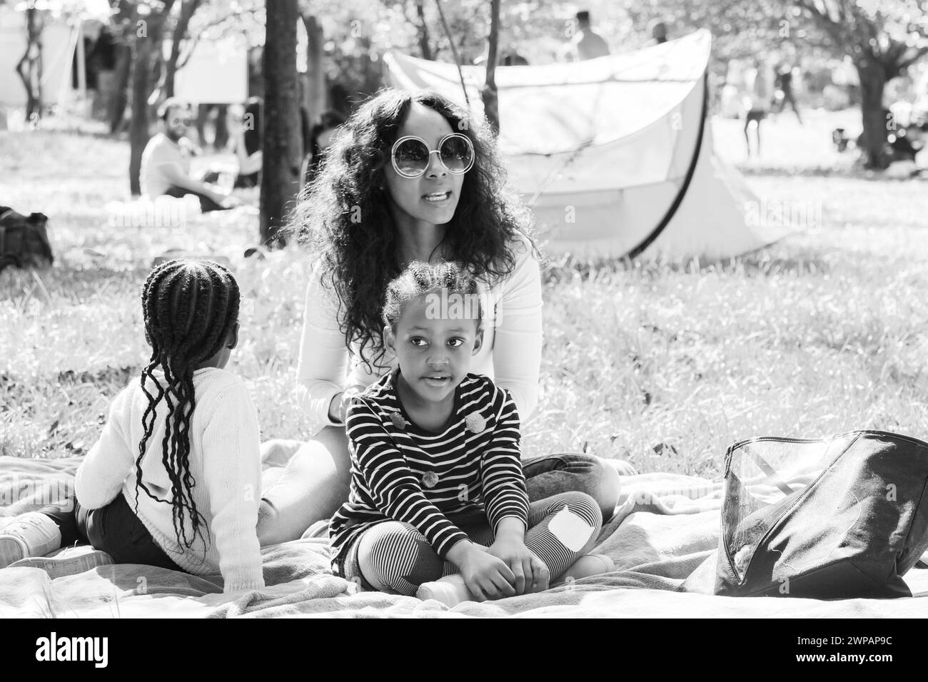 Eine Frau und zwei junge Mädchen sitzen draußen auf einer Picknickdecke Stockfoto