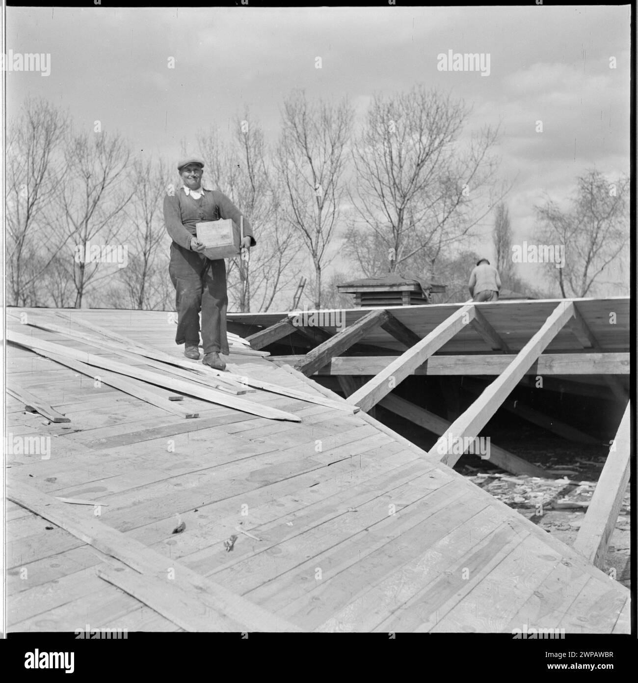 1954 Foto, das Dachdecker auf einem Gebäudedach bei PGR Karsk Pyrzycki zeigt, dokumentiert die ländliche Arbeit der Nachkriegszeit und die frühe Traktorproduktion von Ursus. Stockfoto