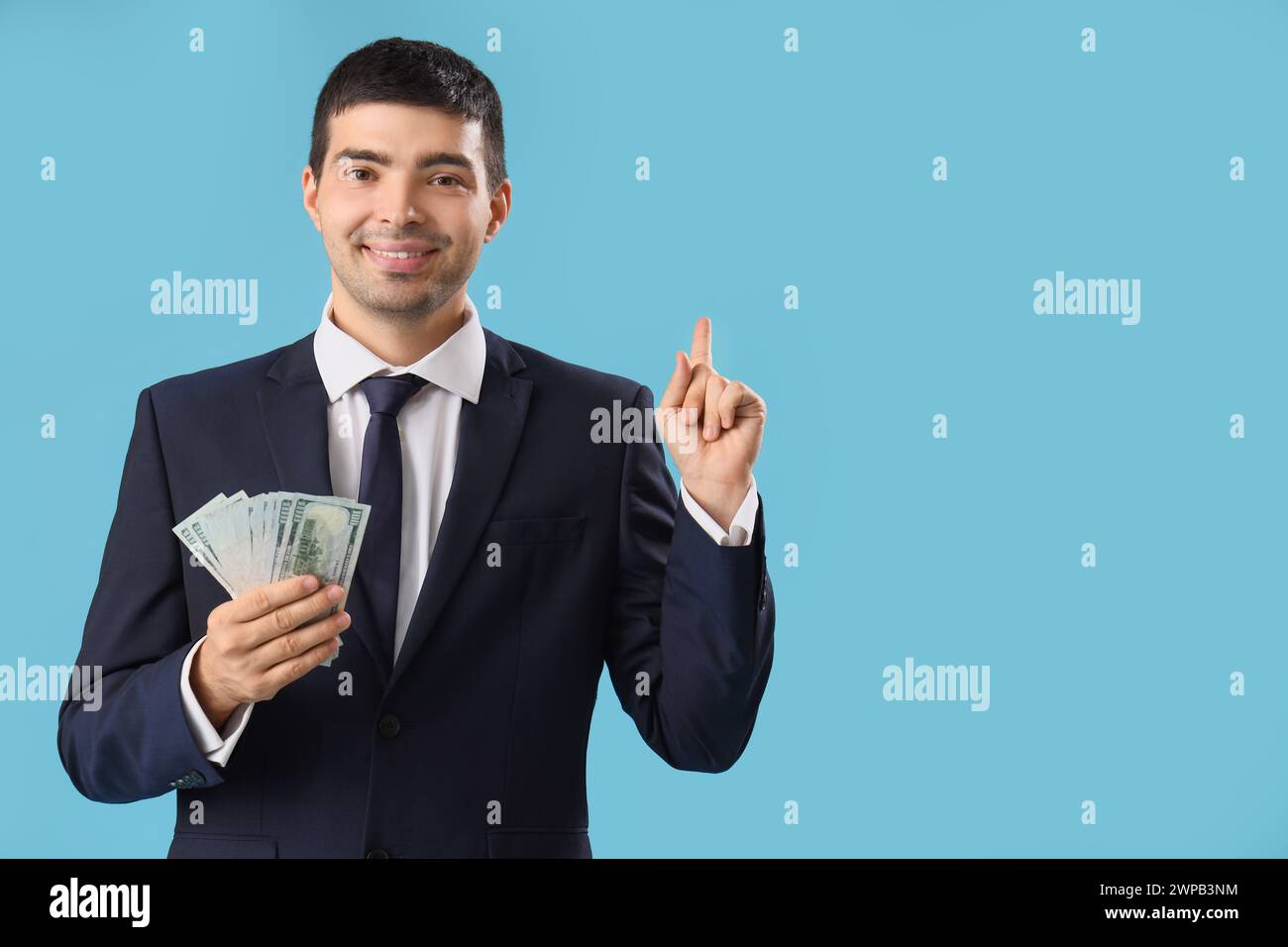 Junger Geschäftsmann mit Geld, der auf etwas auf blauem Hintergrund zeigt Stockfoto