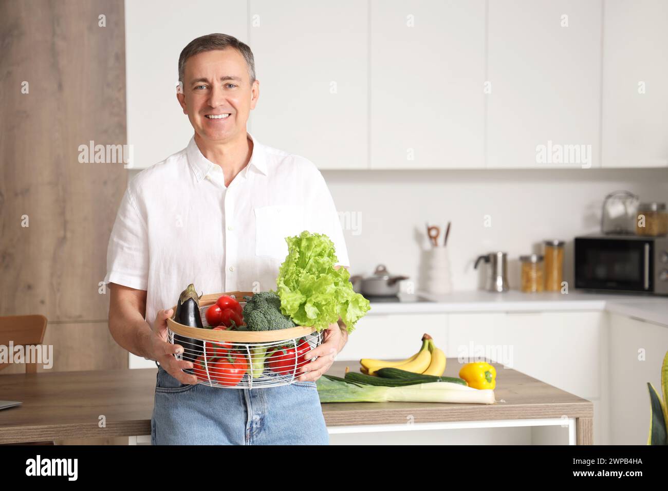 Reifer Mann mit Korb mit frischem Gemüse in der Küche Stockfoto