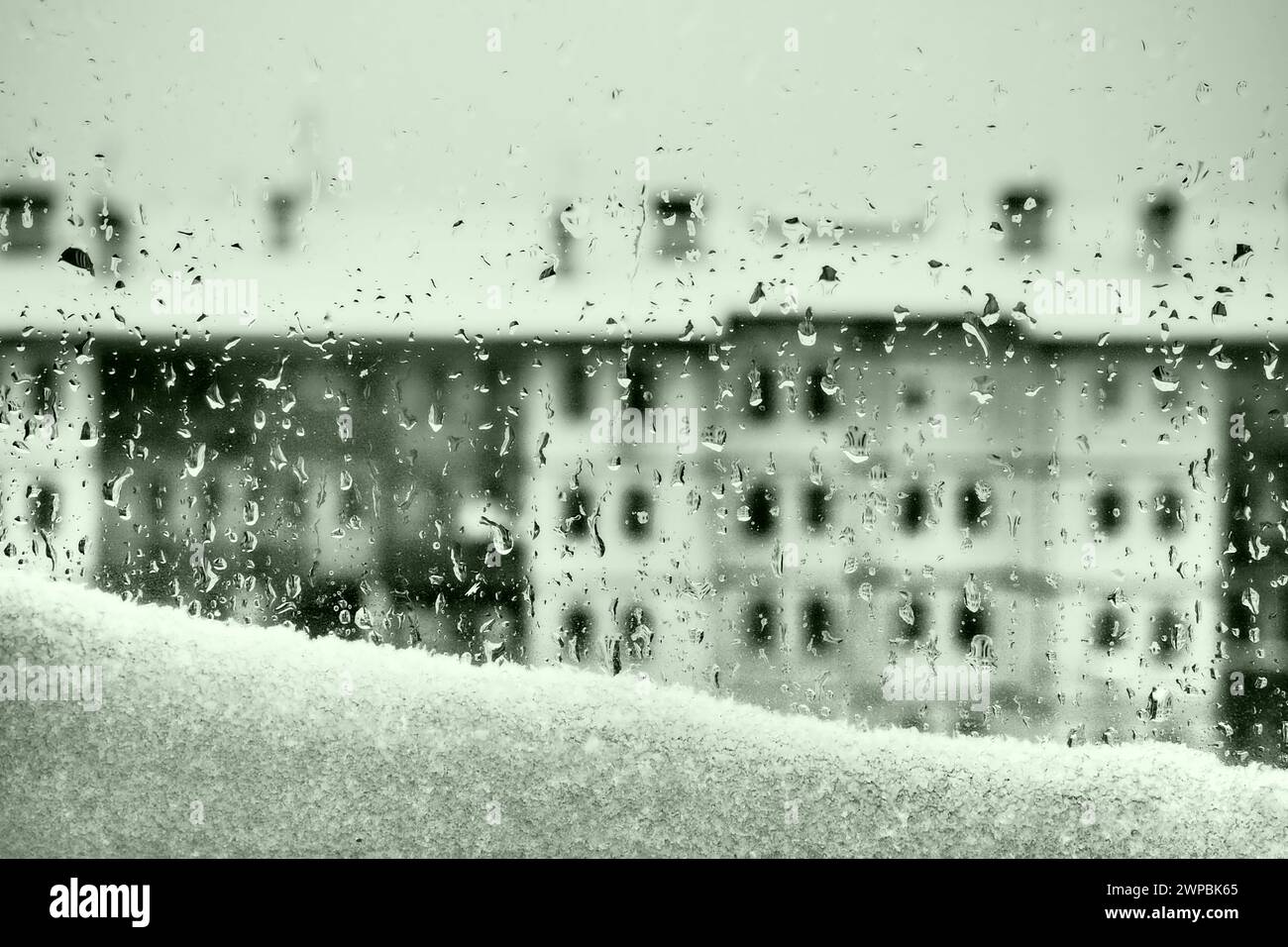 Blick vom Fenster auf das Auftauen im Winter. Schmelzende Schneefräse und Tropfen auf das Glas. Mehrstöckiges Gebäude mit vielen Fenstern. Weihnachten Neujahr Stockfoto