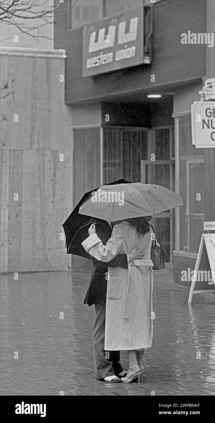 WESTERN Union Schild über einem Paar, das sich unter einem Regenschirm umarmt an einem regnerischen Tag in San Francisco, Kalifornien, 1980er Jahre Stockfoto