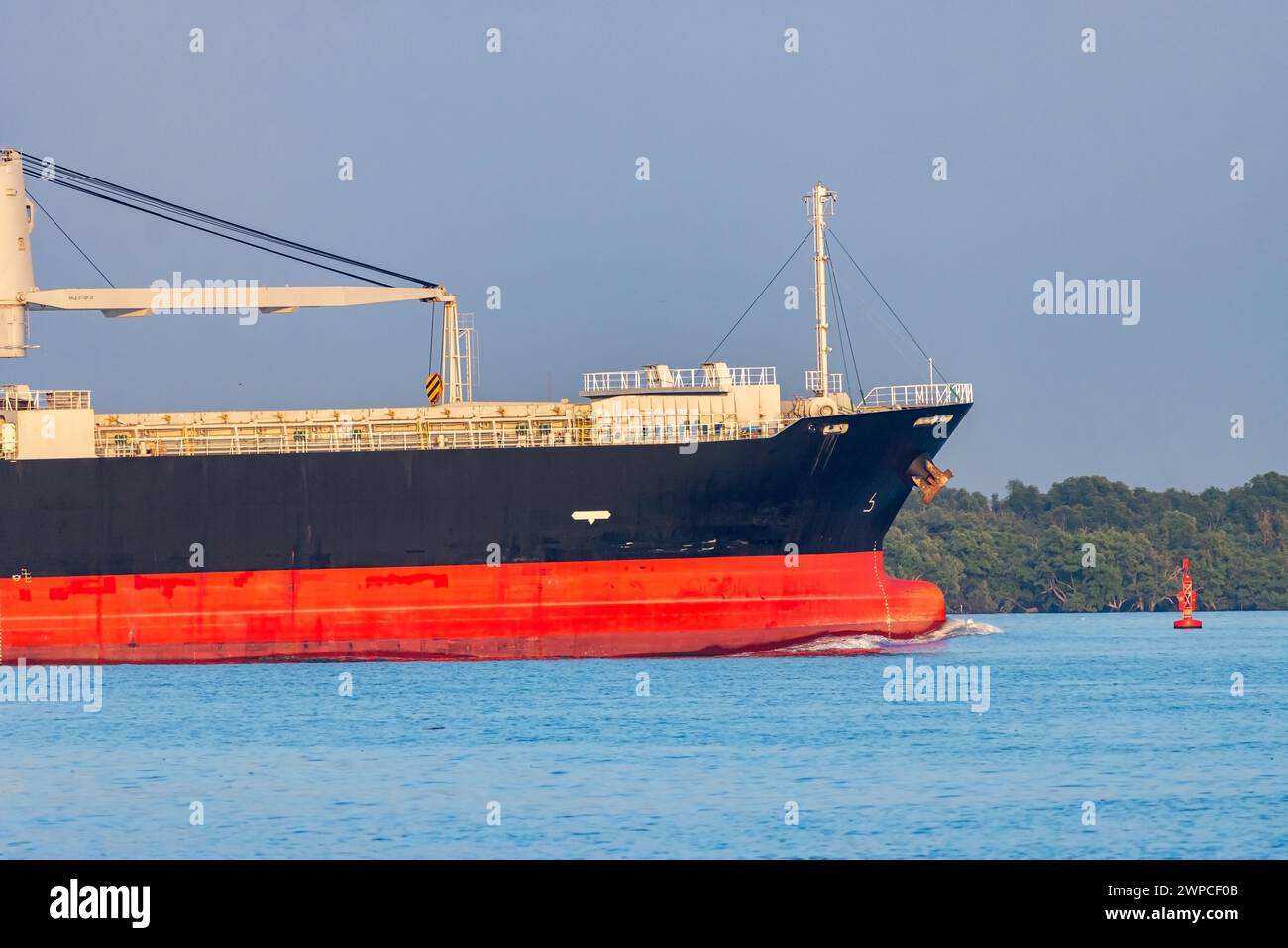 Ein Frachtschiff mit einem Kran fährt entlang der tropischen Küste Stockfoto