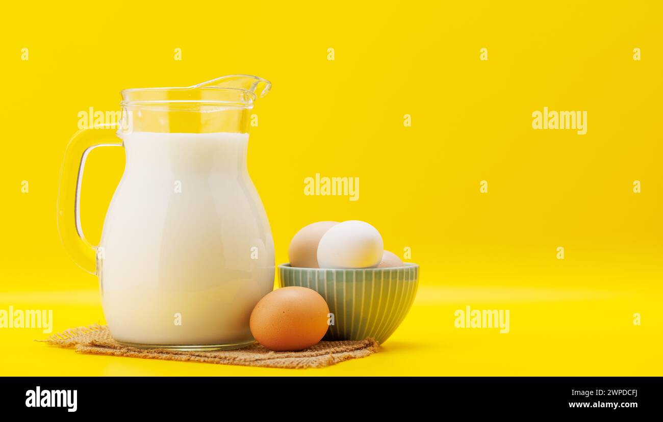 Milchkrug mit Eiern auf gelbem Hintergrund mit Kopierraum Stockfoto