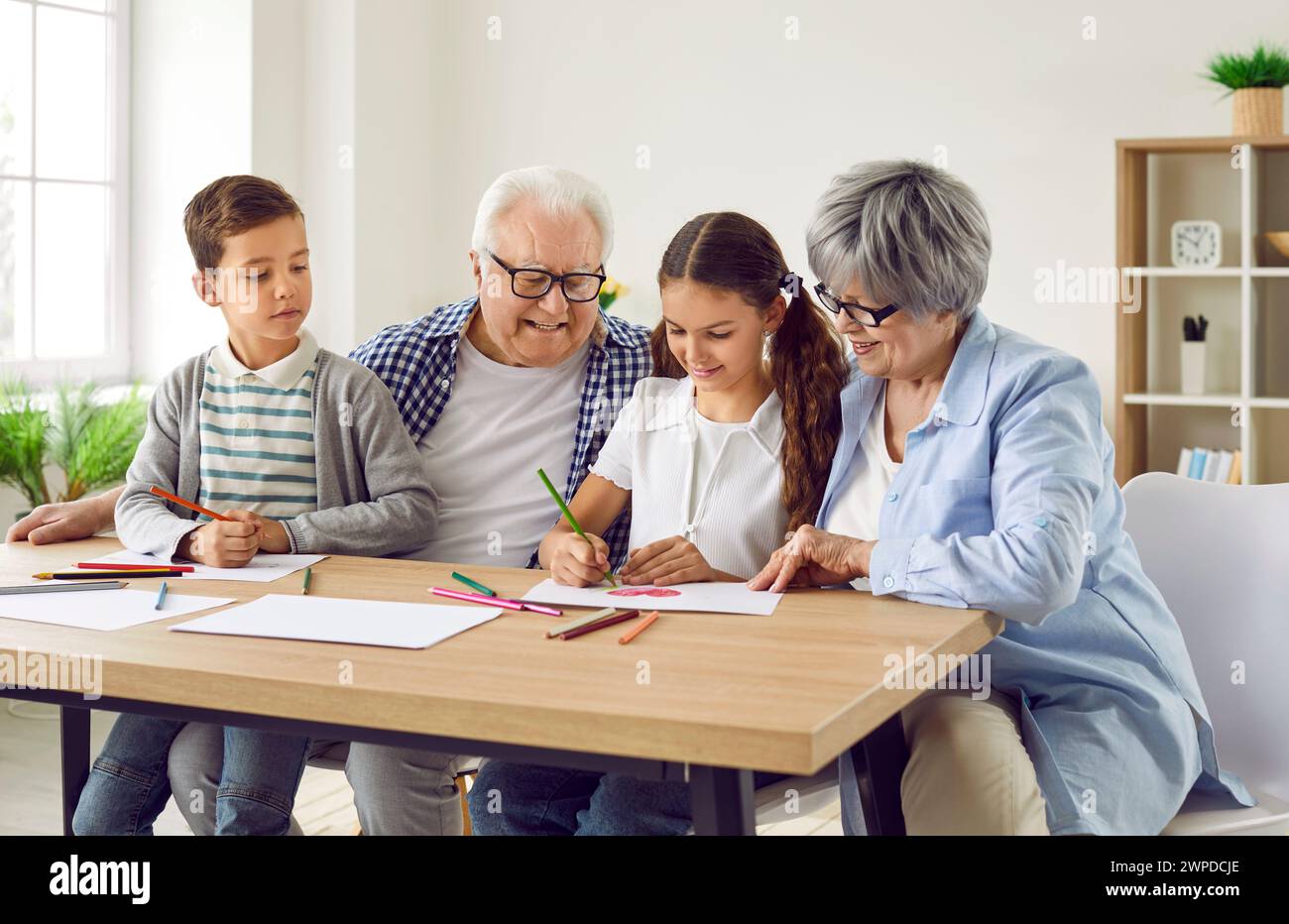 Glückliche Großeltern und Kinder sitzen am Tisch und zeichnen mit Bleistiften auf Papier Stockfoto