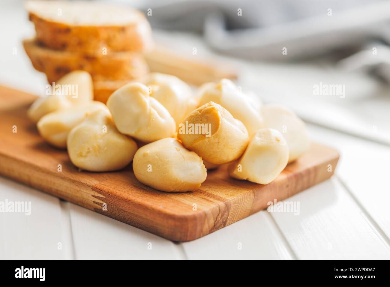 Geräucherter Mini-Scamorza-Käse. Traditioneller italienischer Käse auf Schneidebrett auf dem weißen Tisch. Stockfoto