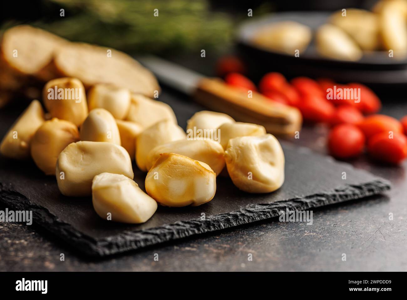 Geräucherter Mini-Scamorza-Käse. Traditioneller italienischer Käse auf Schneidebrett auf dem schwarzen Tisch. Stockfoto