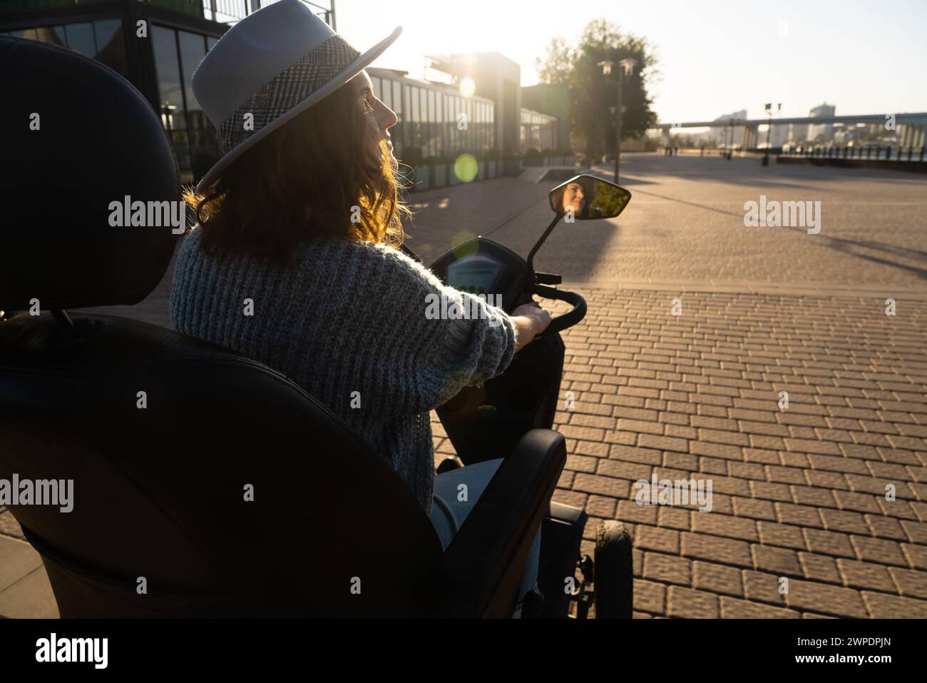Frau Tourist auf einem Elektroroller mit vier Rädern auf einer Stadtstraße. Das Gesicht der Frau ist im Rückspiegel sichtbar. Stockfoto