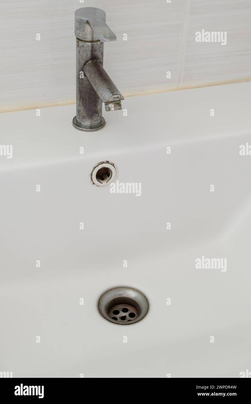 Das Keramikwaschbecken mit dem gebeizten Wasserhahn in der Nähe der weißen Fliesenwand der Toilette im Stadthaus, Vorderansicht für den Hintergrund. Stockfoto
